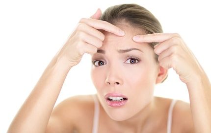 Picture of a woman pointing to a pimple on her forehead