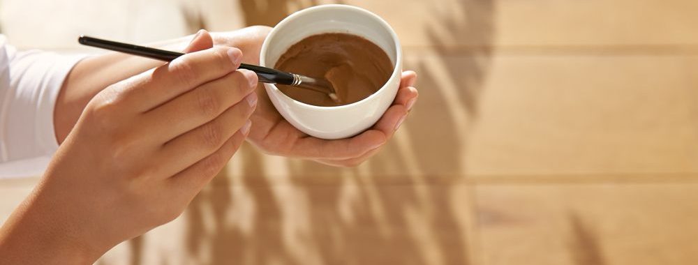 Image of two hands mixing a small bowl of clay mask mixture