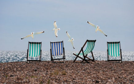 Image of four chairs on the beach with seagulls flying overhead